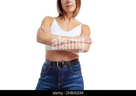 Cropped image of middle-aged woman wearing white top and jeans posing isolated on white studio background. Stock Photo