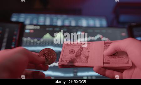 Physical bitcoin shown in red light on stock chart monitor background Stock Photo
