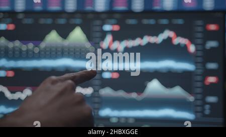 Cryptocurrency exchange, bitcoin and altcoin units long and short on monitors, young adult pointing with index finger Stock Photo