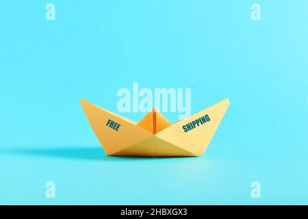 Yellow origami paper ship with the message free shipping on blue background. Free shipping on orders concept. Stock Photo