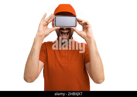 Delivery courier charismatic smiling holds smartphone at face level with both hands on white background Stock Photo