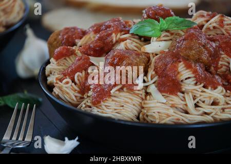 Selective focus of two plates of spaghetti and meatballs pasta with fresh basil leaves and parmesan cheese over a black rustic wood table with blurred Stock Photo