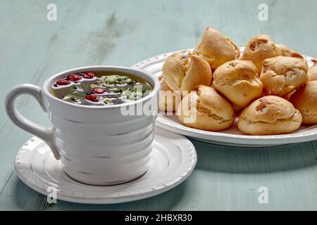 Appetizing profiteroles with whipped cream and a cup of herbal tea Stock Photo