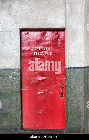 A red barrier fire door in a museum, notice Fire Door Keep Closed, dents and marks on the metal Stock Photo