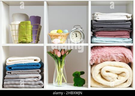 Stacks of towels sheets bed linen blankets pillows on a white shelf. Organization of storage. Easter celebration Stock Photo