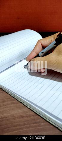 A man's hand holding a pen writing his signature Stock Photo
