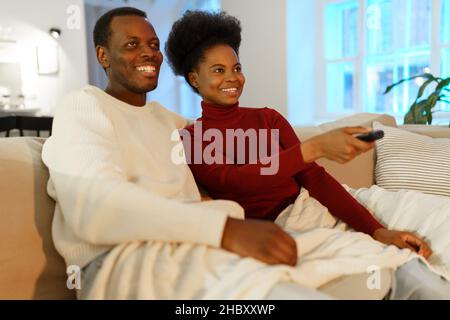 Young happy afro american family couple man and woman watch comedy show on tv and laughing Stock Photo
