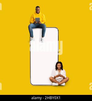 Couple sitting on white empty smartphone screen and using phones Stock Photo