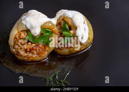2 stuffed yellow bell peppers, with minced pork meat, rice, carrots and onion, sour cream on top, isolated on black background. Stock Photo