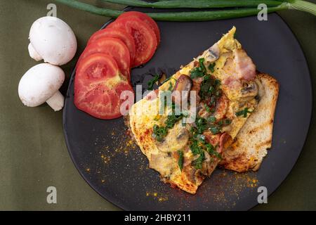 Rustic omelette made with mushrooms and spring onions, sprinkled with smoked paprika and curcuma, on a slice of grilled bread. Raw mushrooms Stock Photo