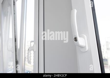 Opened white plastic window handle in upright position close-up. New tilt and turn pvc windows ventilation. Stock Photo