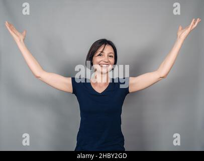 Dark-haired optimistic woman raises her hands in joy and surprise. Happy in anticipation of the surprise. Stock Photo