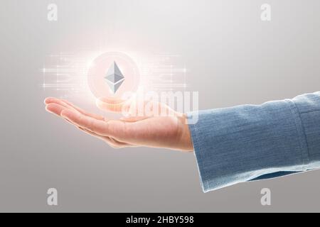 Businesswoman holding abstract glowing cryptocurrency or digital coin sign on a grey background, Ethereum (ETH), Online banking and Crypto Investing c Stock Photo