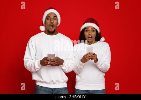 Shocked black couple in Santa hats using mobile phones Stock Photo