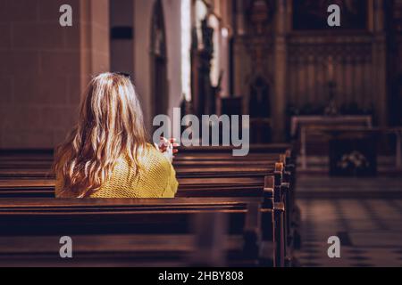 Young woman praying and meditating in church. Belief in Jesus Christ. Catholic cathedral with symbol of religion Stock Photo