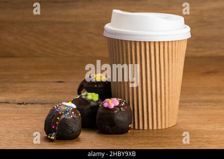 Chocolate balls or choc balls topping with multicolored rainbow sprinkles and colored sugar flower with paper cup of coffee on wooden table. Stock Photo