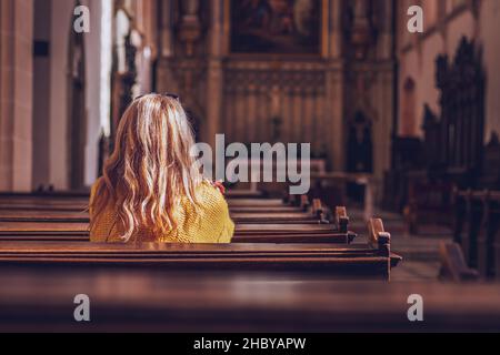 Young woman praying and meditating in church. Belief in Jesus Christ. Catholic cathedral with symbol of religion Stock Photo