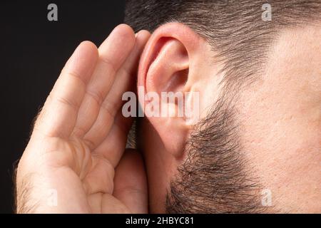 Close-up of man ear with palm listening and collecting rumors. Concept of secret or sense organs, hearing. Stock Photo