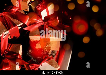 Festive boxes with gifts tied with red ribbon on dark background, orange bokeh Stock Photo