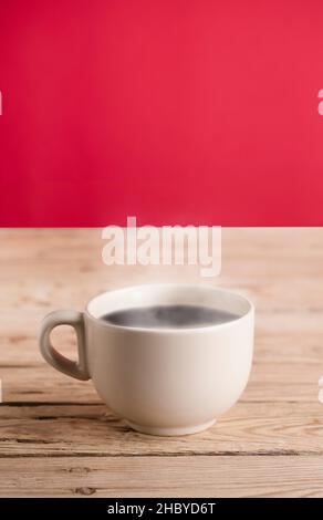 broken white coffee cup with hot steam smoke on rustic wooden table, red background Stock Photo