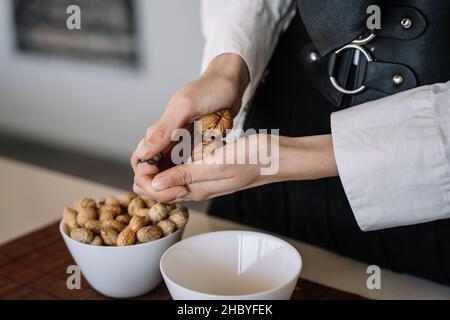 close-up view of a person cracking two walnuts with her hands, blurred horizontal background Stock Photo