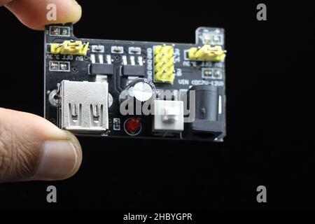 Breadboard power supply module held in hand isolated on black background Stock Photo