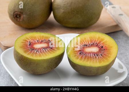 Fresh halved sweet red kiwi on a plate close up and whole ones in the background Stock Photo