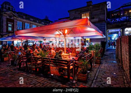 People socialising, eating and drinking in the evening outside at a bar in Covent Garden, London WC2 under a canopy with space heating Stock Photo