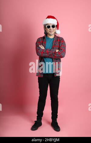 The senior Asian man with Christmas hat standing on the pink background. Stock Photo