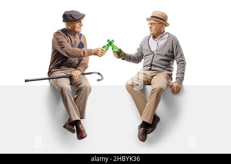 Elderly men sitting on a blank panel and toasting with beer bottles isolated on white background Stock Photo