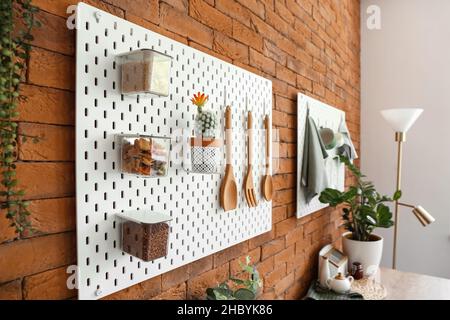 Peg board with kitchenware, cactus and food hanging on brick wall Stock Photo
