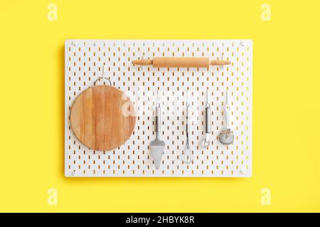 Peg board with kitchenware hanging on yellow wall Stock Photo