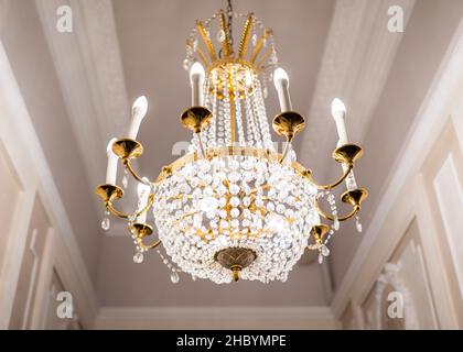 Beautiful chandelier hanging from ceiling. Classic gold plated design with glass crystals. Bright lights viewed from below with classy glass expensive Stock Photo