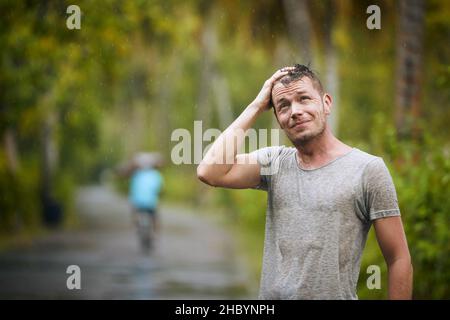 Portrait of drenched young man enjoying heavy rain in nature. Stock Photo