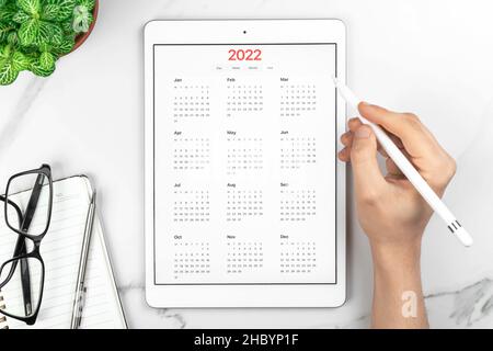 Calendar 2022. Reminder and management concept. Tablet computer with open app. White marble background, business desktop, to do goals and planning for Stock Photo