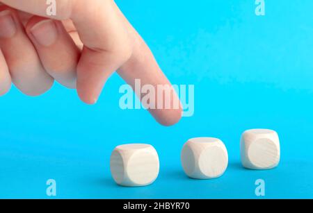 Finger pointing at one of three blank plain wooden blocks, group of cubes. Man choosing, selecting, deciding, picking one element from many, hiring se Stock Photo