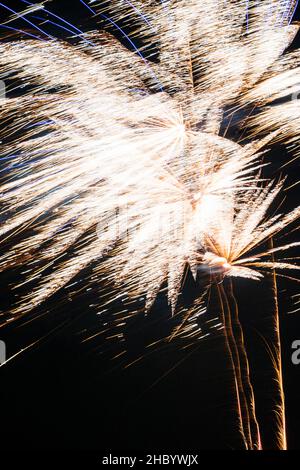 Close up of firework exploding on top of a golden fiery trail in the sky giving an abstract blurry pattern. Motion blur against black nighttime sky. Stock Photo