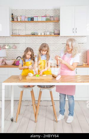 Smiling caucasian mom teaching daughters to cook together in the kitchen. Stock Photo