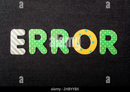 Card with Error word made from mixed vivid colored wooden letters on a textured dark black textile material that can be used as a message Stock Photo