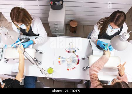 Photo from above of two professional manicurist making holiday manicure for two client women in beauty salon on pandemic time. Stock Photo
