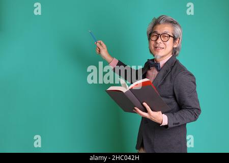 The senior Asian teacher standing on the green background. Stock Photo