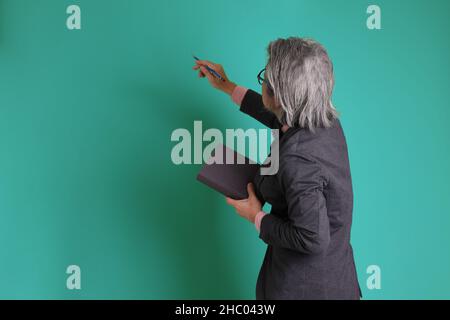 The senior Asian teacher standing on the green background. Stock Photo