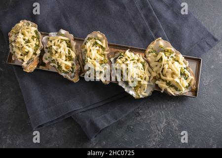 Prepared oysters with herb crust and cheese ready for baking in the oven, dark gray slate background, copy space, high angle view from above, selected Stock Photo