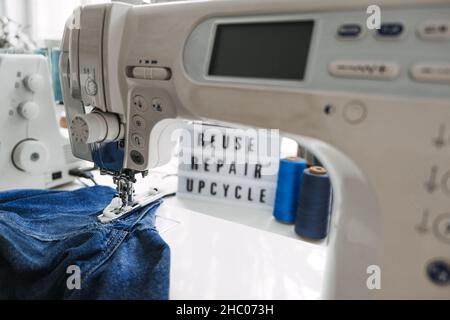 Reuse, repair, upcycle text on light board on sewing machines with old blue jeans, Denim clothes, scissors, thread and sewing tools in sewing studio Stock Photo