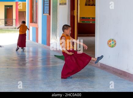 A young Buddhist monk kicks a soccer ball at the Pema Tsal Sakya Monastery near Pokhara, Nepal.  Behind is another boy riding a razor scooter. Stock Photo