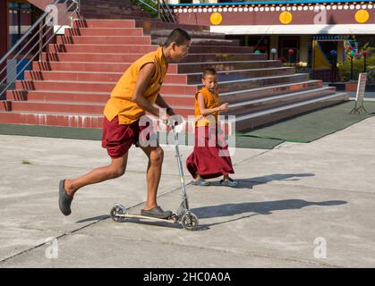 A young Buddhist monk riding a scooter at the Pema Tsal Sakya Monastery near Pokhara, Nepal.  A younger boy follows. Stock Photo