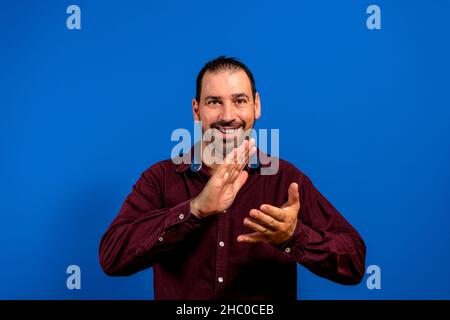 Young handsome man feeling happy and successful, smiling and clapping hands, saying congratulations with an applause against blue wall Stock Photo