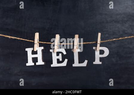 Word HELP with clothespins on black background. Inscription from white letters. Stock Photo