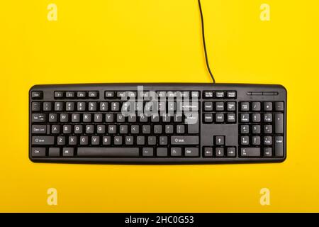 Black keyboard on bright yellow background. Wired computer keyboard. Top view Stock Photo