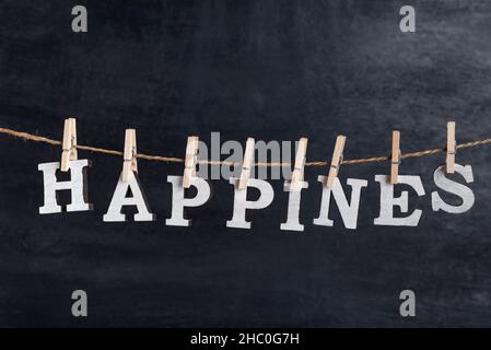 Word HAPPINES held on a clothespin on a rope against black background. Inscription from white letters Stock Photo